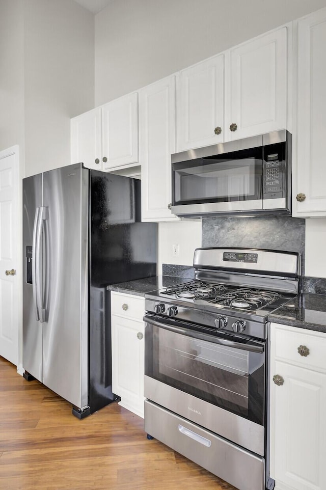 kitchen with stainless steel appliances, white cabinetry, backsplash, and light hardwood / wood-style floors