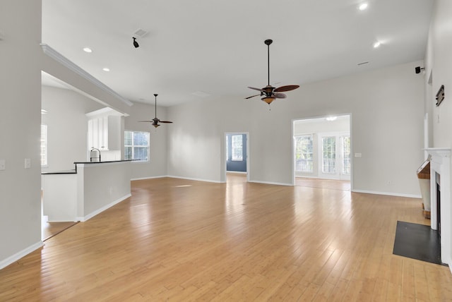 unfurnished living room featuring ceiling fan, plenty of natural light, sink, and light wood-type flooring