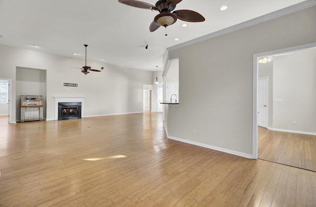 unfurnished living room featuring ceiling fan, crown molding, and light wood-type flooring