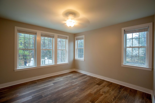 empty room with a healthy amount of sunlight, baseboards, and dark wood-style flooring