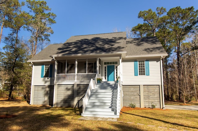 coastal inspired home with a front yard, roof with shingles, stairs, and a sunroom