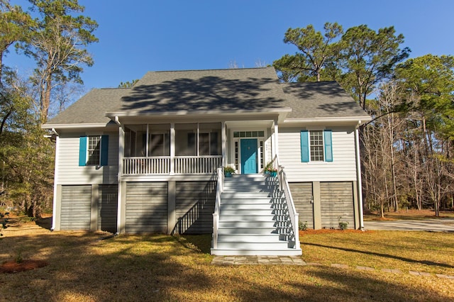 coastal home featuring a shingled roof, stairs, a front lawn, and a sunroom