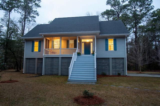 raised beach house with stairway, roof with shingles, covered porch, and a front lawn