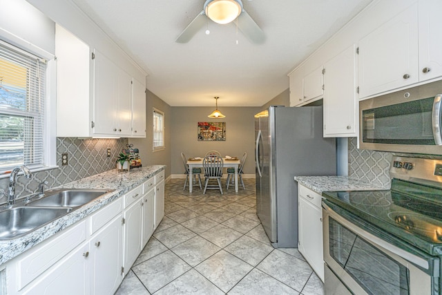 kitchen featuring sink, appliances with stainless steel finishes, white cabinetry, a wealth of natural light, and decorative light fixtures