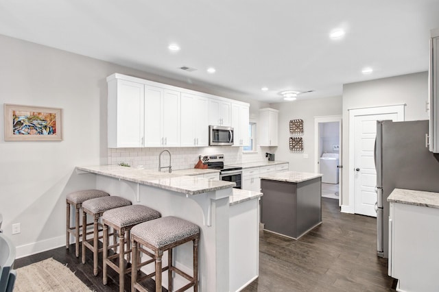6190 Button Bush Dr, Ravenel, SC 29470 - kitchen with appliances with stainless steel finishes, washer / clothes dryer, a peninsula, decorative backsplash, and dark wood-type flooring
