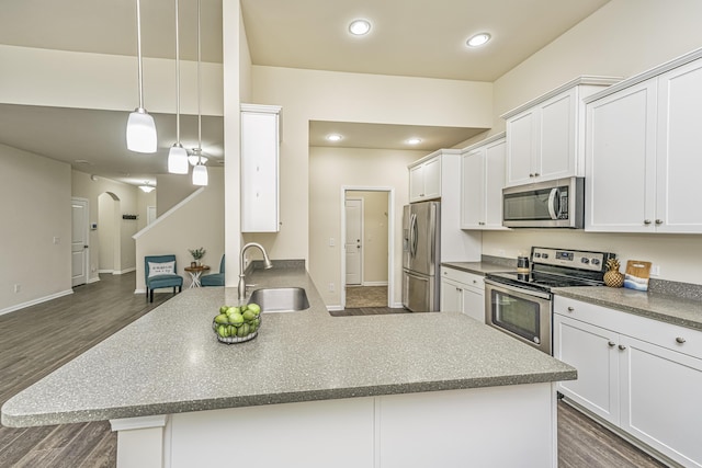 kitchen with a sink, arched walkways, stainless steel appliances, a peninsula, and dark wood-type flooring