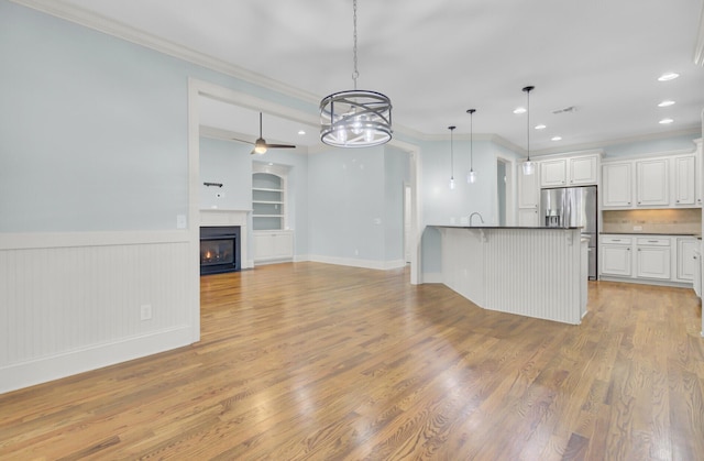 kitchen with light wood-type flooring, dark countertops, stainless steel fridge with ice dispenser, and crown molding