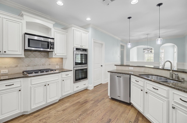 kitchen with arched walkways, a sink, stainless steel appliances, crown molding, and light wood-type flooring