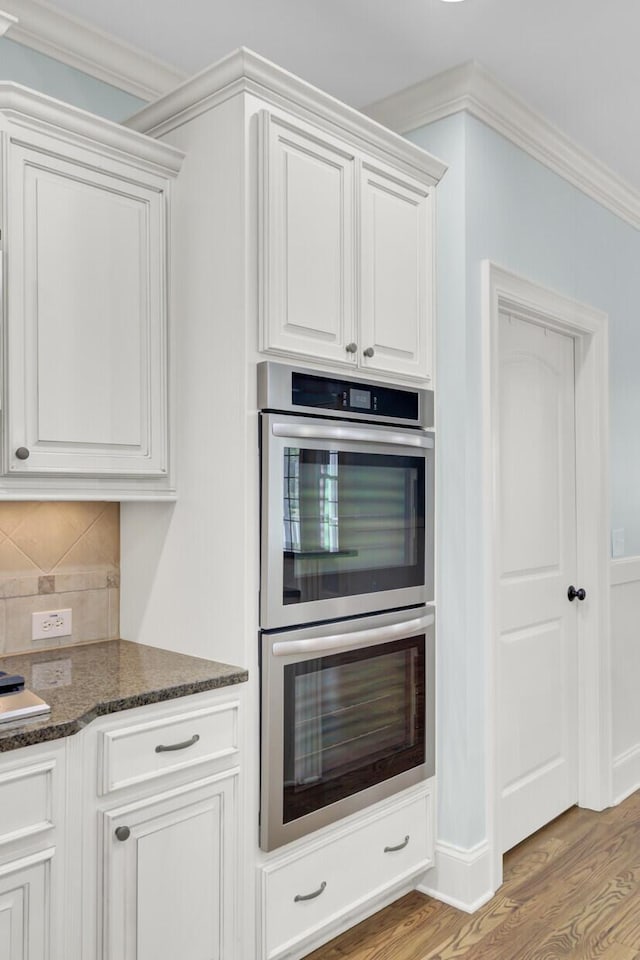 kitchen with dark stone countertops, wood finished floors, stainless steel double oven, decorative backsplash, and white cabinets