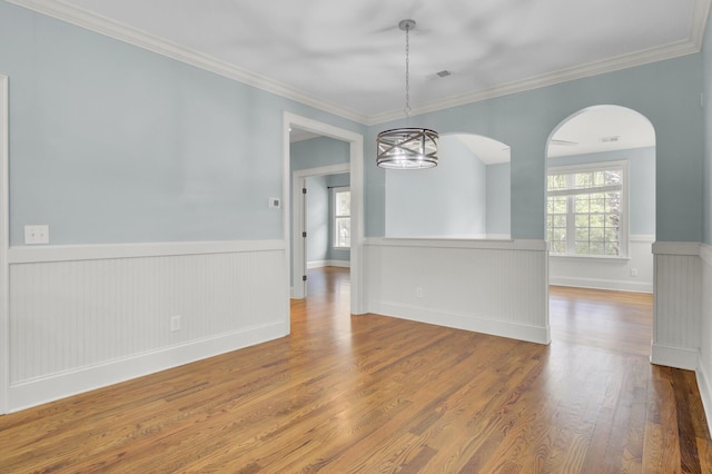 unfurnished dining area featuring an inviting chandelier, wood finished floors, wainscoting, and ornamental molding