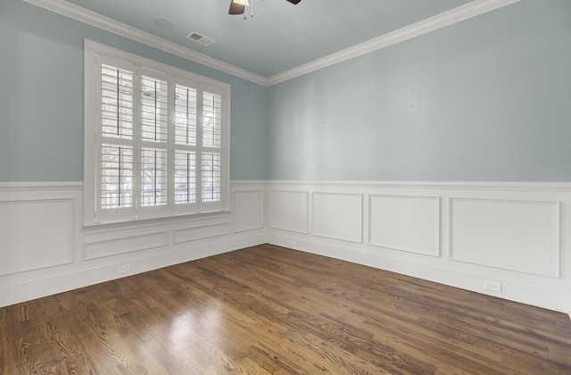 spare room featuring a ceiling fan, a wainscoted wall, visible vents, dark wood finished floors, and ornamental molding