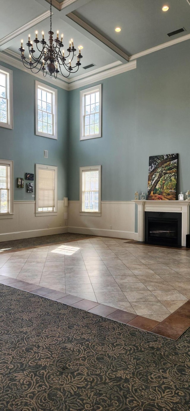 tiled foyer entrance with an inviting chandelier, a wainscoted wall, a towering ceiling, and ornamental molding