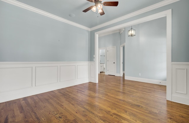 empty room with wainscoting, wood finished floors, a ceiling fan, and crown molding