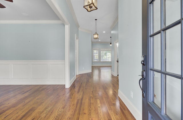 foyer entrance with a wainscoted wall, ceiling fan with notable chandelier, wood finished floors, crown molding, and a decorative wall