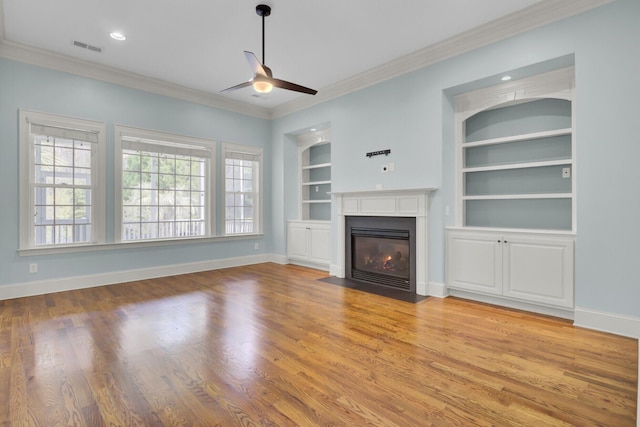 unfurnished living room featuring visible vents, built in shelves, crown molding, baseboards, and ceiling fan