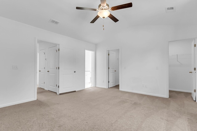 unfurnished bedroom featuring ceiling fan, light colored carpet, lofted ceiling, a walk in closet, and a closet