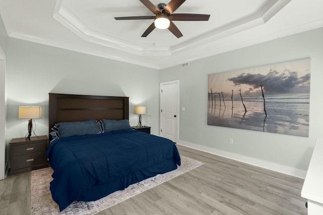 bedroom featuring visible vents, baseboards, a tray ceiling, and wood finished floors