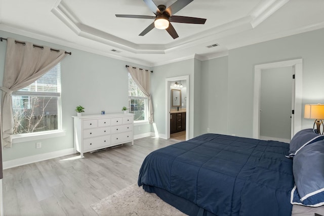 bedroom featuring baseboards, visible vents, a tray ceiling, ensuite bathroom, and light wood-type flooring