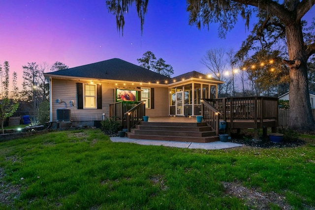 back of house at dusk featuring a deck, a yard, fence, and central AC