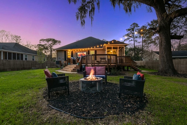 back of house at dusk featuring stairway, a yard, a fenced backyard, a fire pit, and a deck