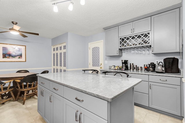 kitchen with light stone counters, gray cabinetry, a textured ceiling, ceiling fan, and a kitchen island