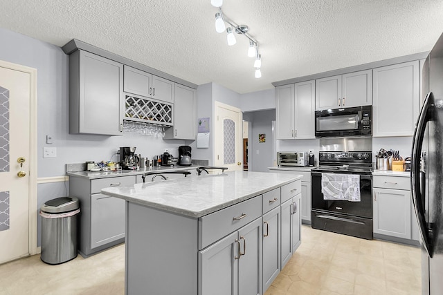 kitchen featuring light stone countertops, a textured ceiling, a kitchen island with sink, black appliances, and gray cabinets