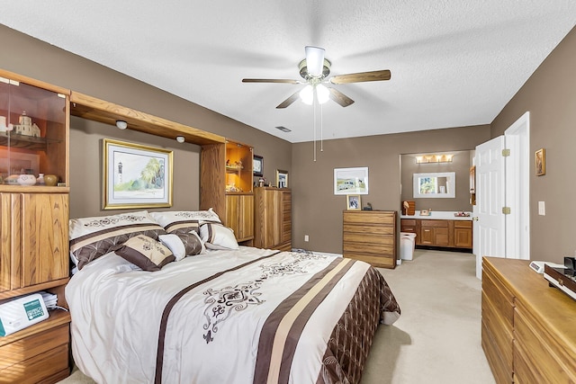 carpeted bedroom featuring a textured ceiling, ensuite bath, and ceiling fan