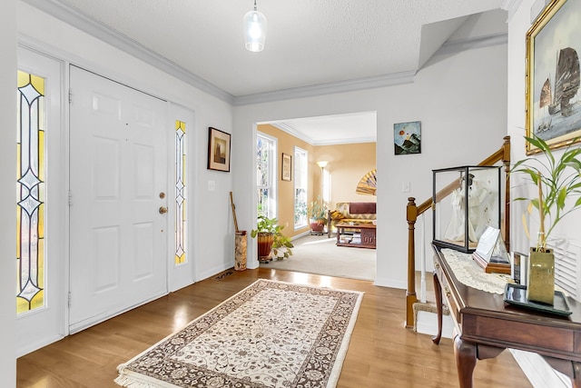 entrance foyer with light wood-type flooring, a textured ceiling, and ornamental molding