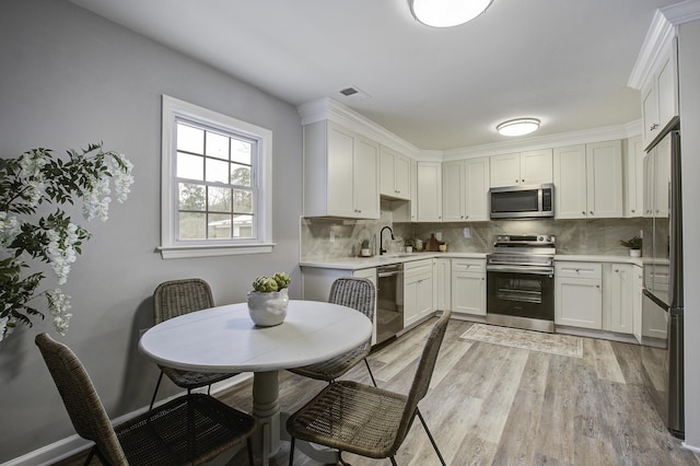 kitchen featuring appliances with stainless steel finishes, tasteful backsplash, white cabinetry, sink, and light wood-type flooring