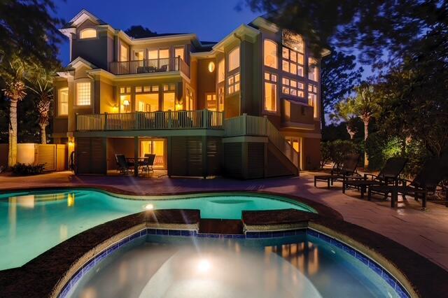 12 Port Tack, Hilton Head Island, SC 29928 - back of house at night with a balcony, stucco siding, a patio area, and a pool with connected hot tub