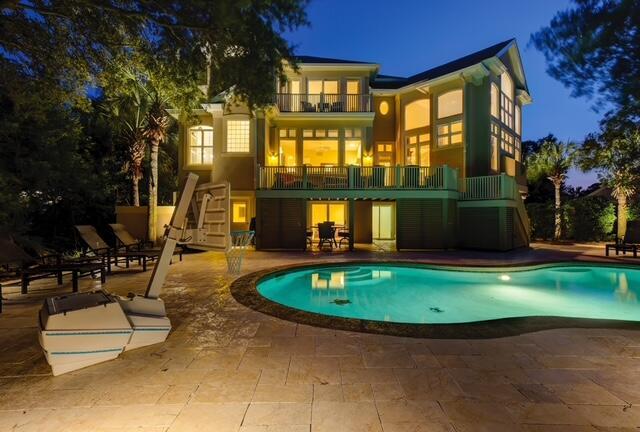 12 Port Tack, Hilton Head Island, SC 29928 - back of house at night with a balcony, a patio, an outdoor pool, and stucco siding