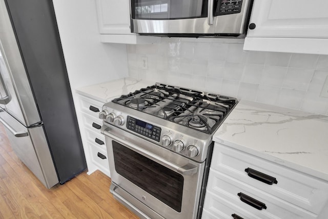 kitchen featuring white cabinets, appliances with stainless steel finishes, light stone countertops, light wood finished floors, and tasteful backsplash