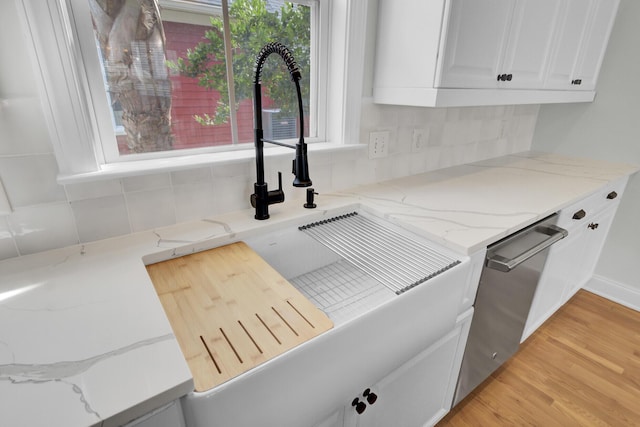 interior details featuring light stone counters, a sink, light wood-style floors, stainless steel dishwasher, and backsplash