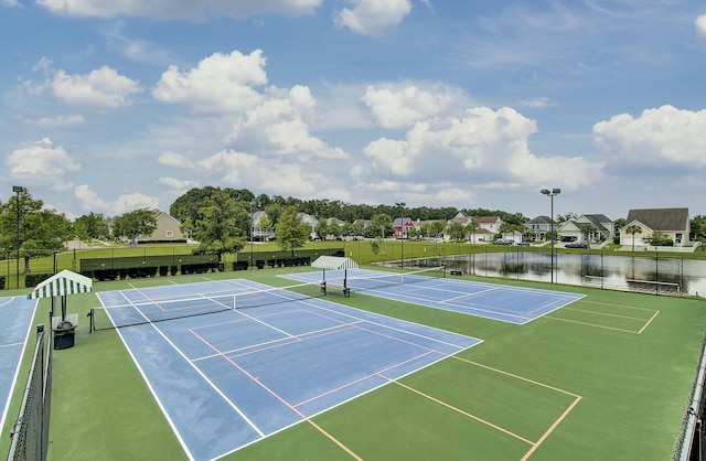 view of tennis court featuring a water view, a residential view, and fence