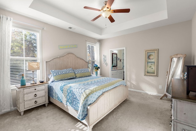 bedroom with ensuite bathroom, ceiling fan, light colored carpet, and a tray ceiling