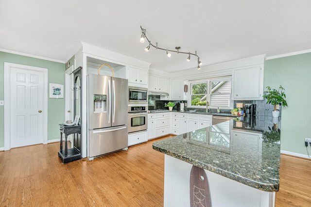 kitchen with crown molding, light hardwood / wood-style flooring, appliances with stainless steel finishes, white cabinetry, and tasteful backsplash