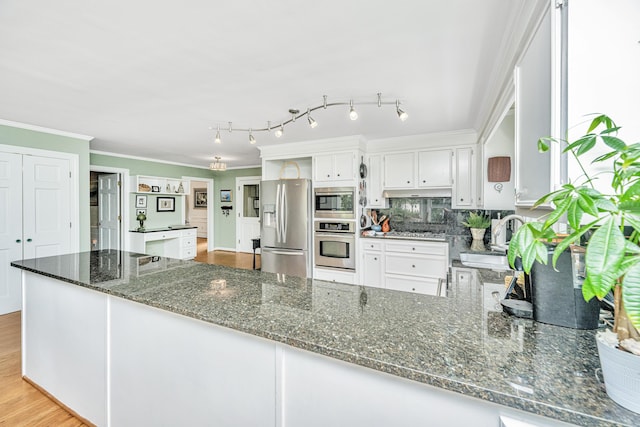 kitchen with appliances with stainless steel finishes, white cabinetry, sink, dark stone countertops, and ornamental molding