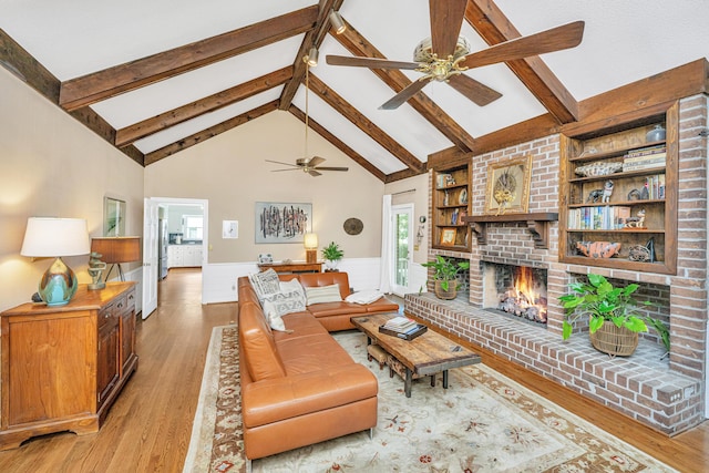 living room featuring a brick fireplace, beam ceiling, built in features, and light hardwood / wood-style floors