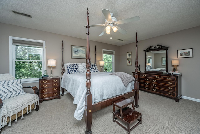 bedroom with multiple windows, light carpet, a textured ceiling, and ceiling fan