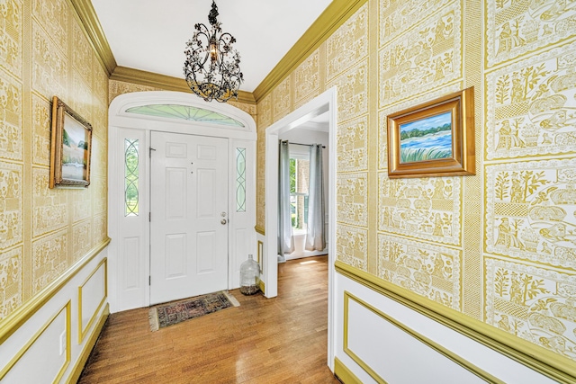 foyer with ornamental molding, a notable chandelier, and light wood-type flooring