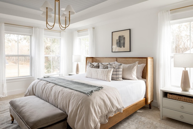 bedroom featuring multiple windows, a tray ceiling, light carpet, and a chandelier