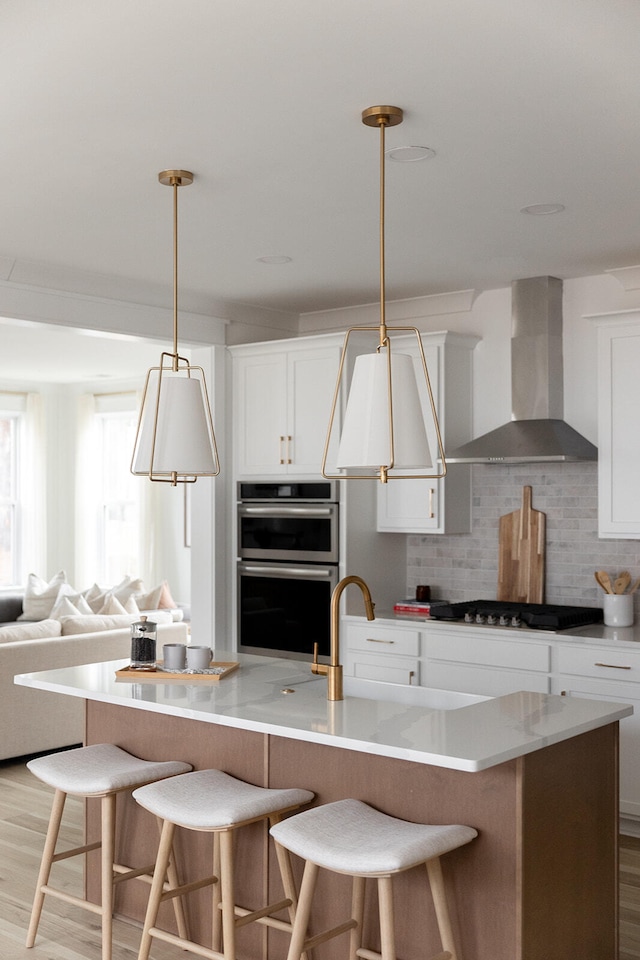 kitchen featuring white cabinets, wall chimney range hood, double oven, gas cooktop, and light hardwood / wood-style floors