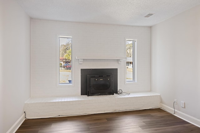 unfurnished living room featuring a healthy amount of sunlight, visible vents, a textured ceiling, and wood finished floors