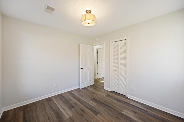 unfurnished bedroom with a closet, dark wood finished floors, visible vents, and baseboards