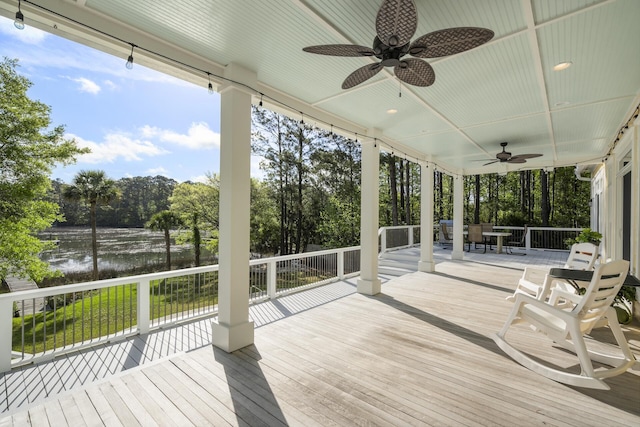 wooden terrace with outdoor dining space, ceiling fan, and a water view