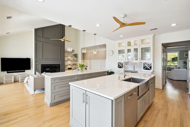 kitchen with sink, gray cabinetry, vaulted ceiling, a center island with sink, and hanging light fixtures