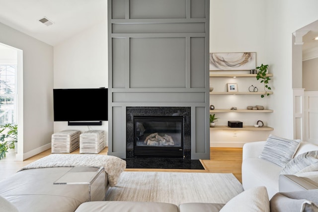 living room with a high end fireplace, vaulted ceiling, and light wood-type flooring