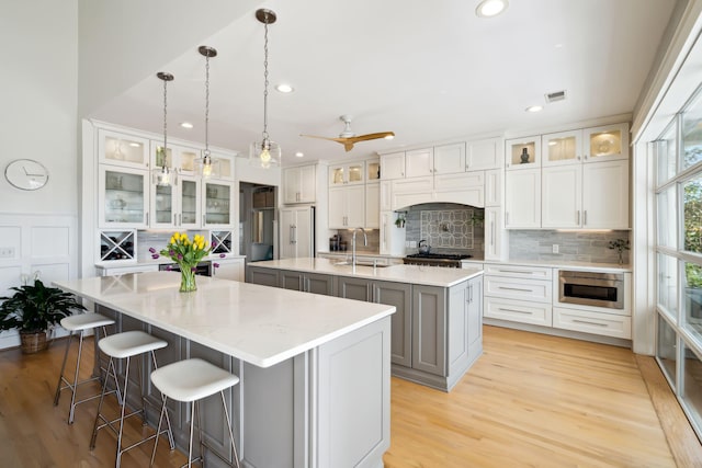 kitchen with pendant lighting, sink, white cabinets, decorative backsplash, and a center island with sink