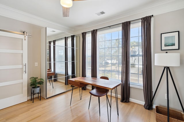 dining area featuring crown molding, light hardwood / wood-style flooring, a barn door, and ceiling fan