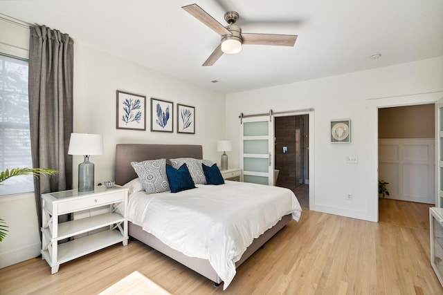 bedroom featuring a barn door, ceiling fan, and light hardwood / wood-style flooring